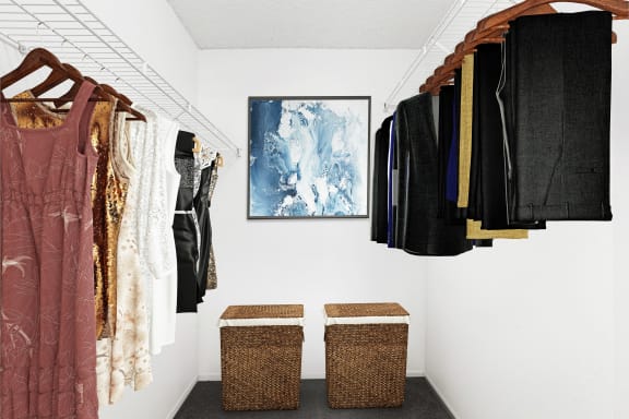 Walk-in closet with clothes hanging from wire shelving with two laundry hampers