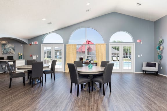 Clubhouse interior with hardwood style flooring two sets of round tables with chairs and business center in the background