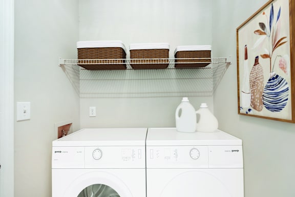 A white front loading washing machine with a shelf above it.