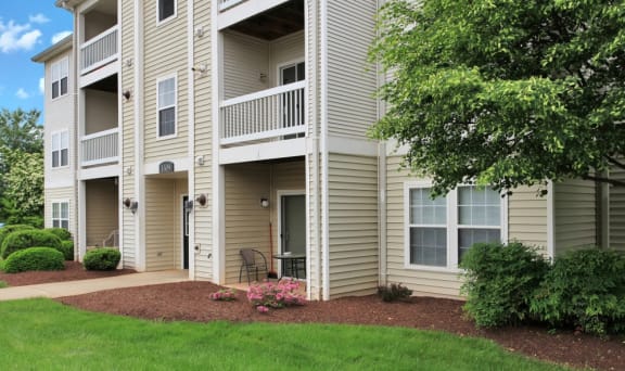 Exterior of apartment with patio and flower beds with tree.