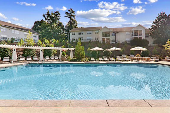 a swimming pool with lounge chairs and umbrellas in front of a building at Caveness Farms Apartments, North Carolina, 27587