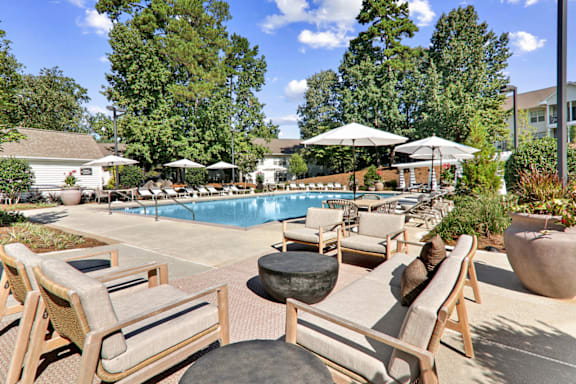 a swimming pool with lounge chairs and umbrellas at Caveness Farms Apartments, Wake Forest, NC 27587
