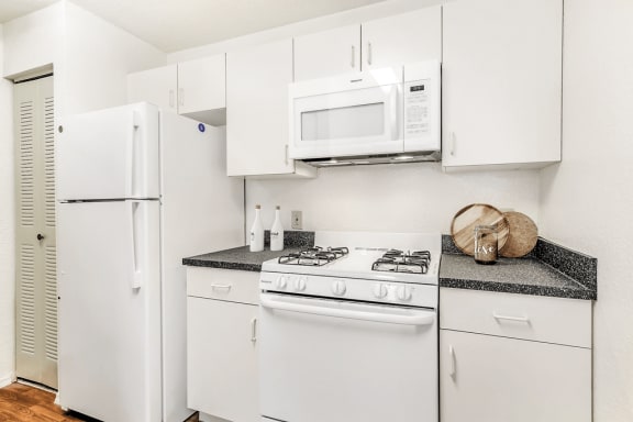 Virtually staged kitchen with white appliances, wood flooring, gas stove and white cabinetry