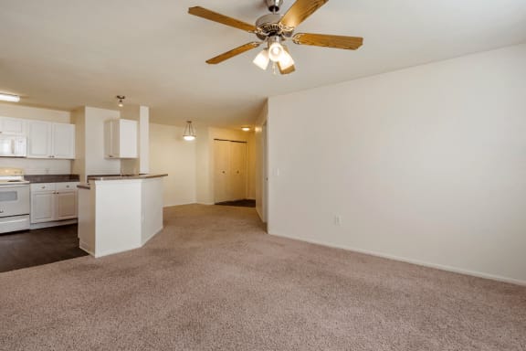 Living room with carpet flooring, multi speed ceiling fan, and kitchen with hardwood style flooring