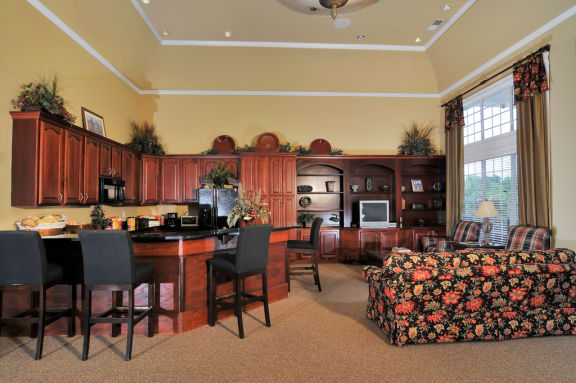 Resident clubhouse with ample seating. Cabinets line the back wall with bar stools surrounding the bar top table.