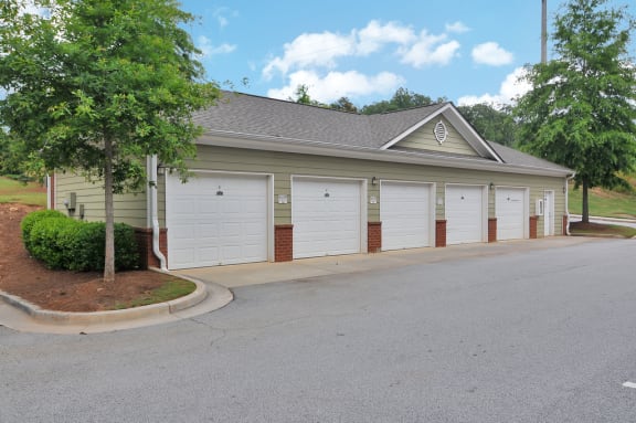 Detached resident garages. Five garages side by side with white doors and a vinyl siding surround. Trees on both ends.