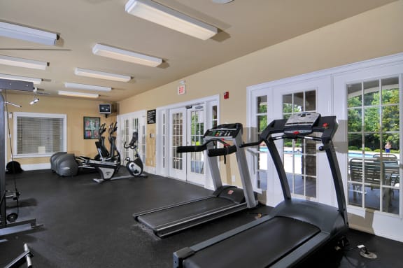 Resident fitness center with treadmills, ellipticals, and stationary bikes. Windows overlook the pool.