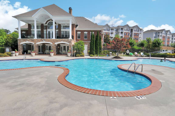 Community pool with pool furniture throughout. The clubhouse is in the background, surrounded by trees.