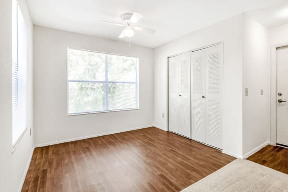 A study with hardwood-style floors, a ceiling fan, windows, and a closet, near the entryway into the apartment.