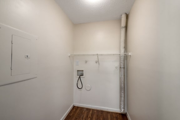 The laundry room features full-size washer and dryer connections with hardwood-style flooring, white walls, and ceiling. There is also a shelf located above the washer and dryer connections.