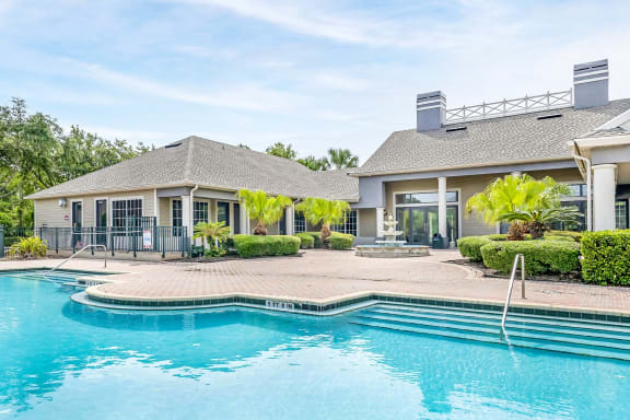 Swimming pool with sundeck, shrubs, and the exterior of the clubhouse.