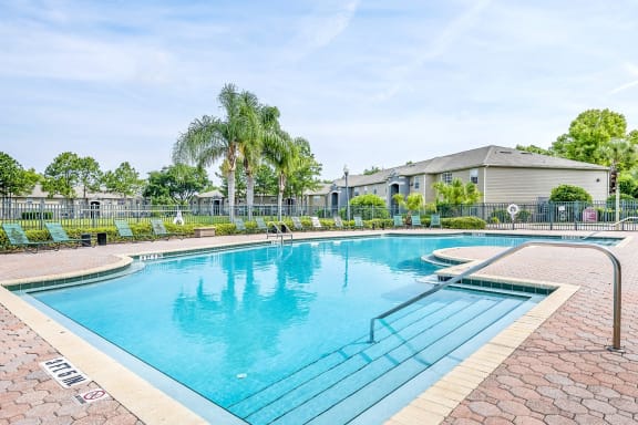 Swimming pool with a brick paver sundeck, palm trees, and lounge chairs.