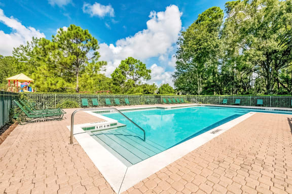 Swimming pool with a brick paver sundeck and lounge chairs.