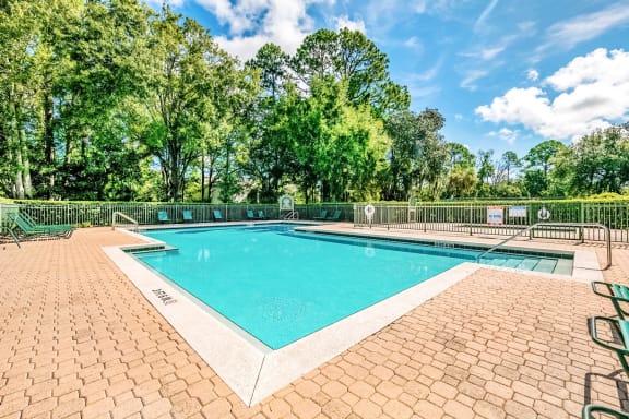 Swimming pool with a brick paver sundeck and lounge chairs.