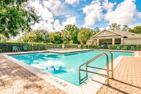 Swimming pool with a brick paver sundeck and lounge chairs outside the clubhouse.