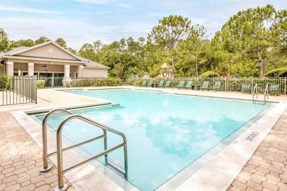 Swimming pool with a brick paver sundeck and lounge chairs outside the clubhouse.