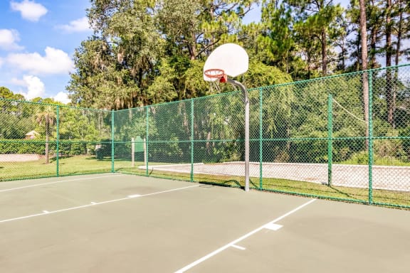 A fenced-in basketball court adjacent to a sand volleyball court.