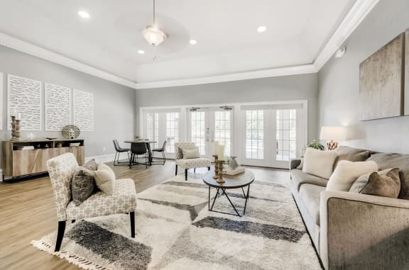 Clubhouse with a seating area, dining table, and four chairs, with hardwood-style flooring and large windows.