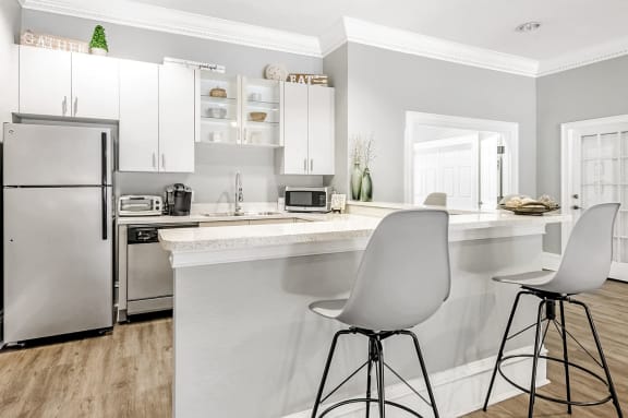 Clubhouse kitchen with white cabinets, white countertops, and a breakfast bar with two barstools.