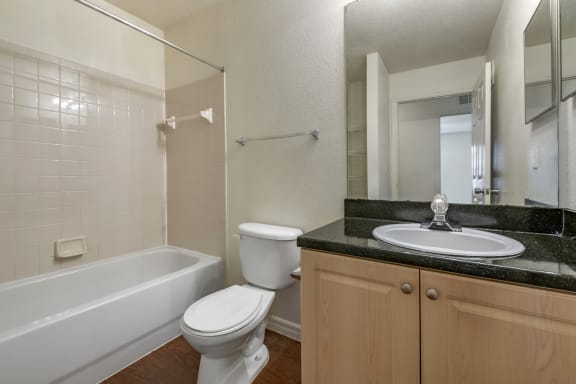 Bathroom with Blonde Cabinets, Black Counters and White Bathtub and Beige Shower