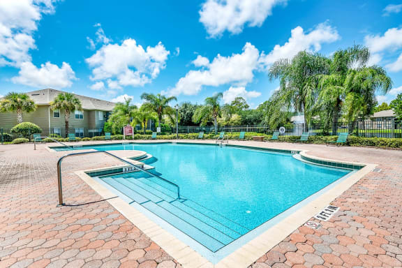 Swimming pool with a brick paver sundeck, palm trees, and lounge chairs.