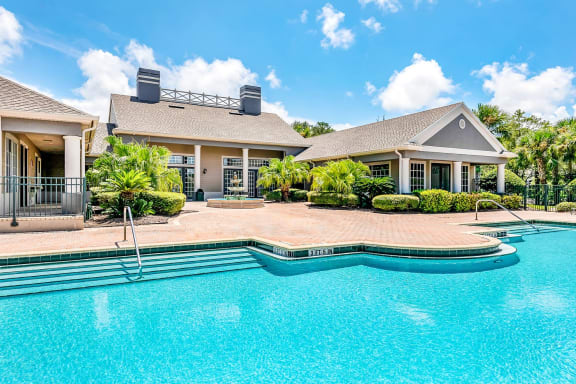 Swimming pool with a brick paver pool deck and shrubs outside the clubhouse.