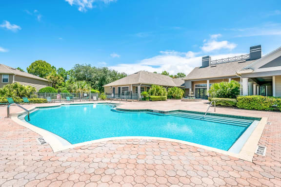 Swimming pool with a brick paver sundeck, palm trees, and lounge chairs.