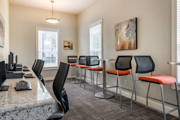 Clubhouse business center with computers, chairs, desk, and large windows for natural lighting