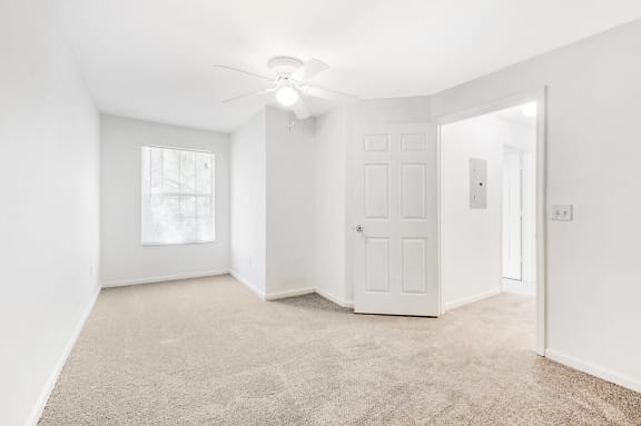 Vacant bedroom with white walls,  carpet, window, and a ceiling fan.