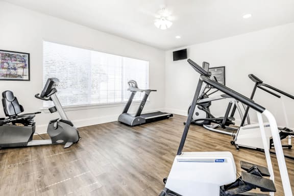 Fitness center with cardio machines and large window with wall mounted television and ceiling fan with light