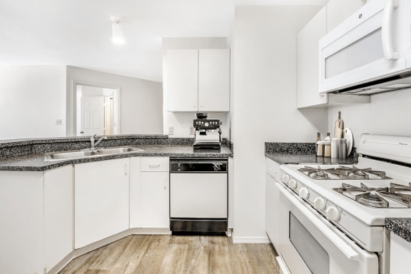 Virtually staged kitchen with white cabinets, gray countertop, white appliances, gas stove and wood flooring