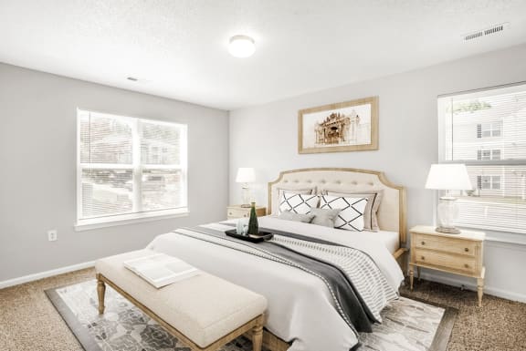 The vacant bedroom features tan carpet throughout with beige walls and a white textured ceiling. Windows are located on the right and left sides of the room providing ample natural light and feature blinds on both.