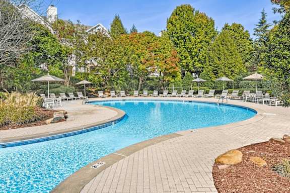 A large outdoor swimming pool surrounded by trees and chairs.