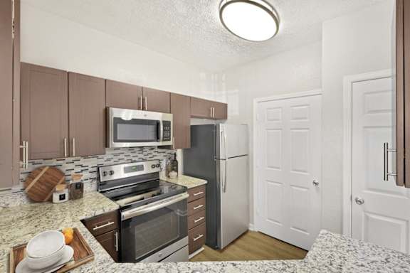 A kitchen with a refrigerator, oven, and microwave.