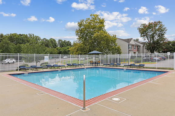 A pool surrounded by a white fence with trees in the background.