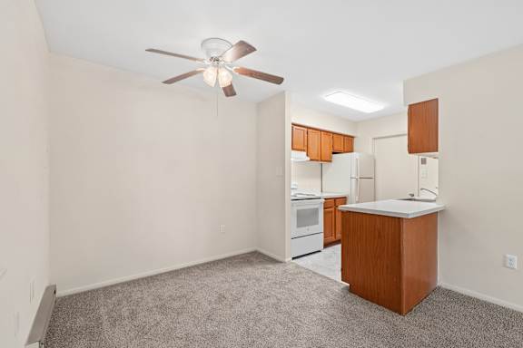 A room with a ceiling fan and a kitchenette.