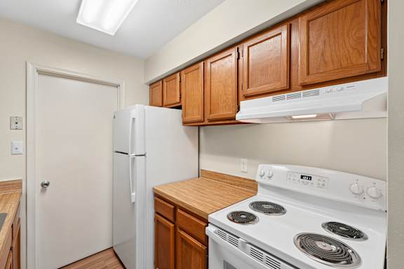 A kitchen with a white stove top oven and white refrigerator.