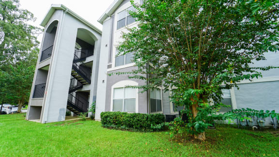 an apartment building with a green lawn and tree in front of it