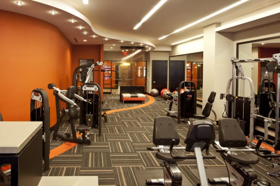 Fitness center with weighted equipment and full size mirrors against wall with orange accent colors