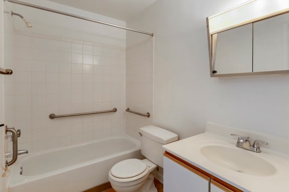 Bathroom with White Cabinets White Counters and White Bathtub and Shower with Handrails