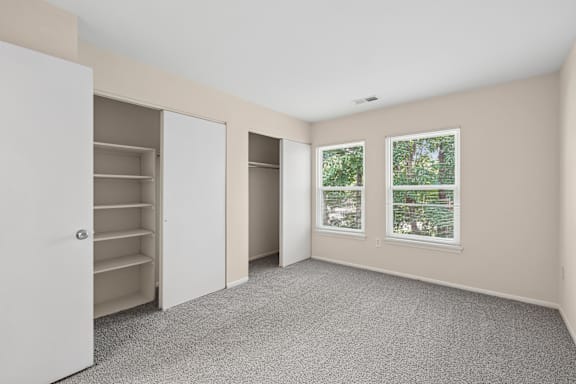 A room with a white door, two windows, and a carpeted floor.
