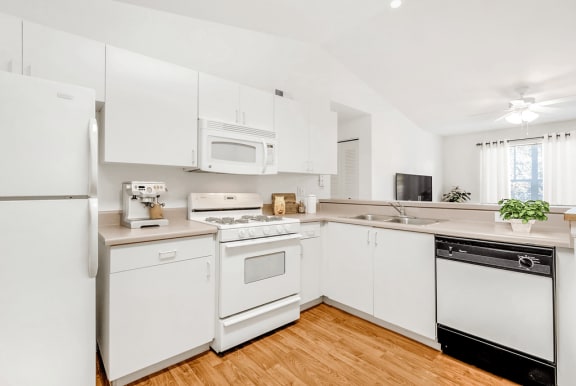 Virtually staged kitchen with white appliances, wood flooring, gas stove, ceiling fan, wall mounted television, dishwasher