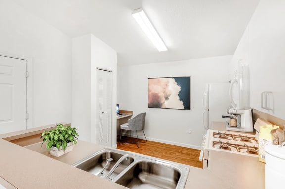 Virtually staged kitchen with white appliances, wood flooring, gas stove, computer desk