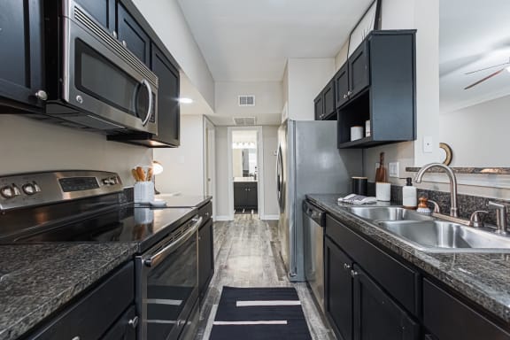 a kitchen with black cabinets, stainless steel appliances and granite-style countertops