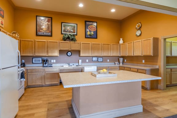 Clubhouse kitchen with wood cabinetry, large island, white appliances and coffee maker with wood style flooring