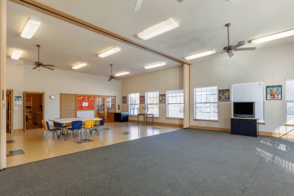 Activity room with tables and chairs, ceiling fan, and tile flooring, sliding partition and carpeted area and television