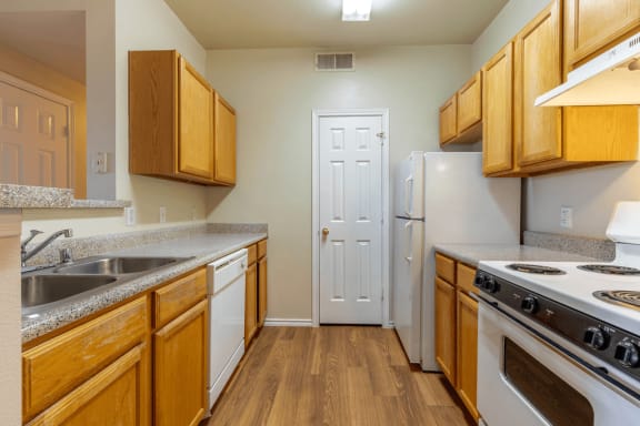 Kitchen with wood cabinetry, wood style flooring, white appliances, double basin sink, pantry door