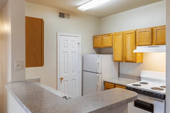 Kitchen with wood cabinetry, white appliances, granite inspired countertops, pantry  door