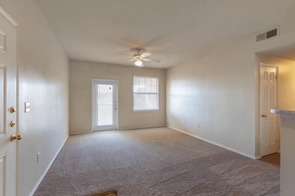 Livingroom with carpet, ceiling fan with light, entry way door, large window with mini blinds, and patio exit door