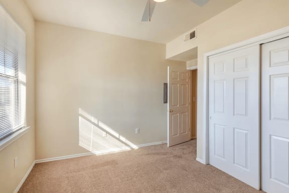 Bedroom with carpet, ceiling fan with light, sliding closet doors and window with mini blinds